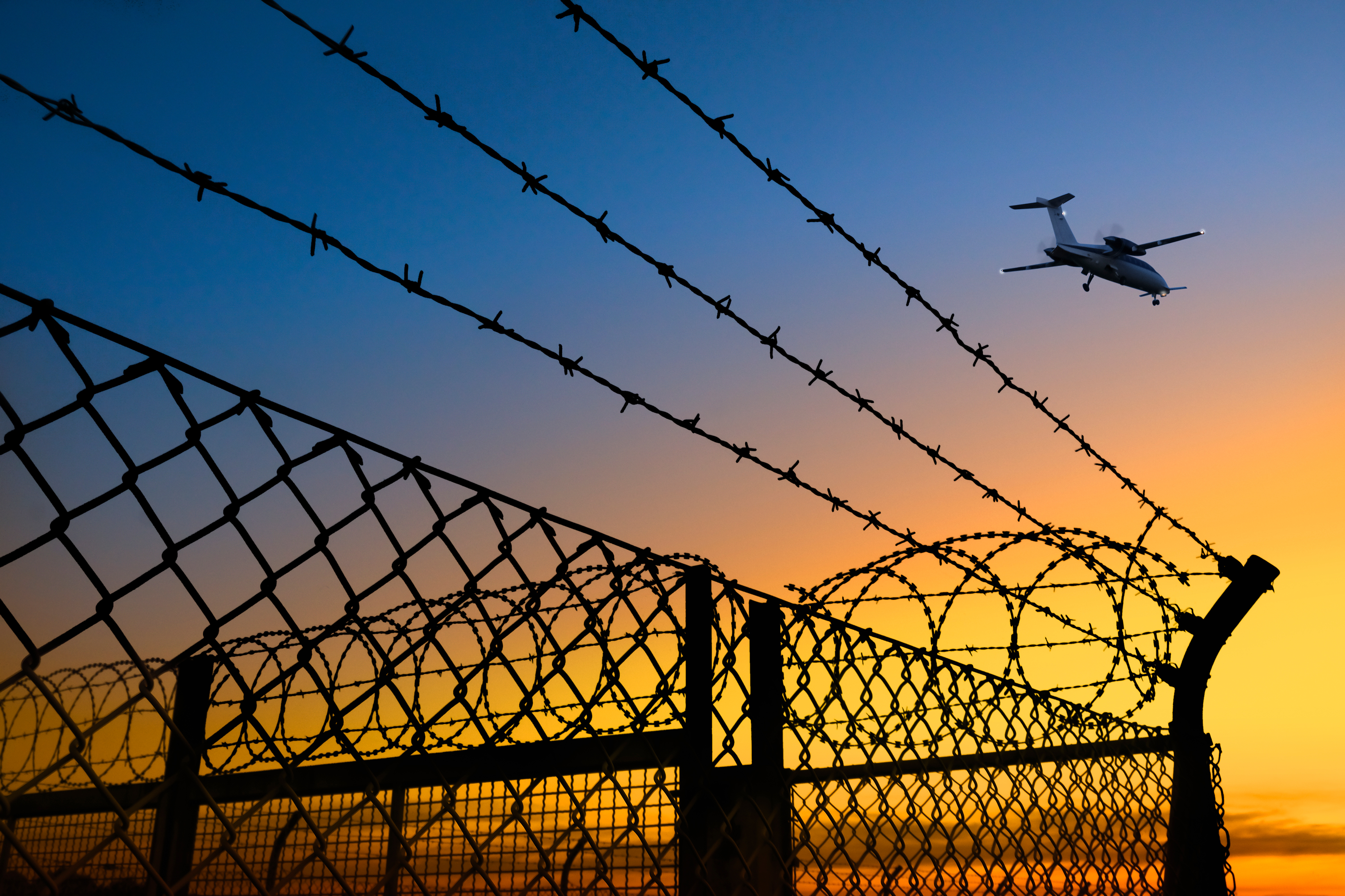 Flugzeug in der Dämmerung über Stacheldrahtzaun