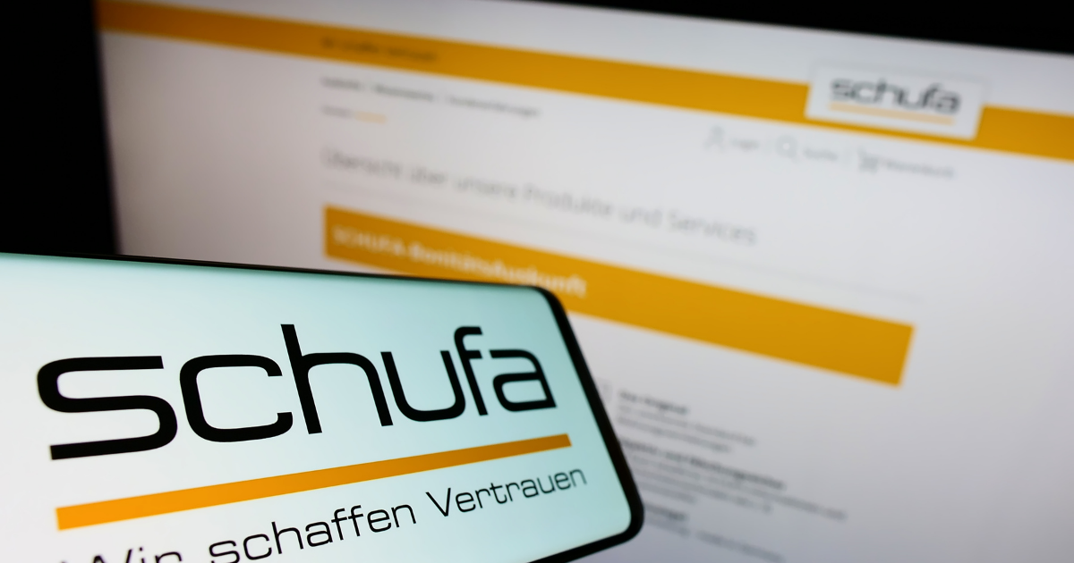 Mobiltelefon mit Logo der Schufa vor Bildschirm mit Schufa-Webseite